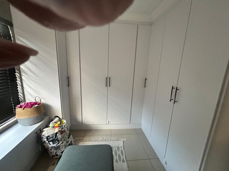 A bedroom featuring white built-in cupboards and tiled flooring, with natural light entering through a window with venetian blinds.