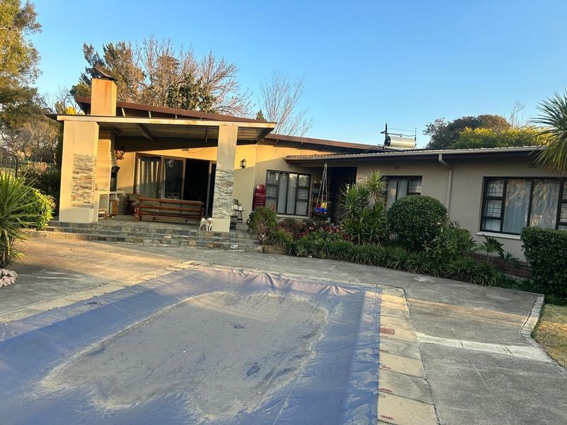 Rear exterior view featuring a covered patio with built-in braai, a swimming pool with cover, and established garden landscaping.