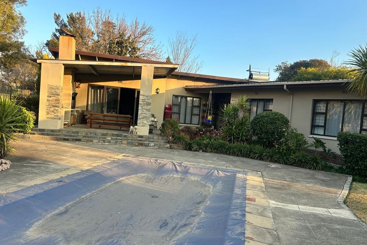Rear exterior view featuring a covered patio with built-in braai, a swimming pool with cover, and established garden landscaping.