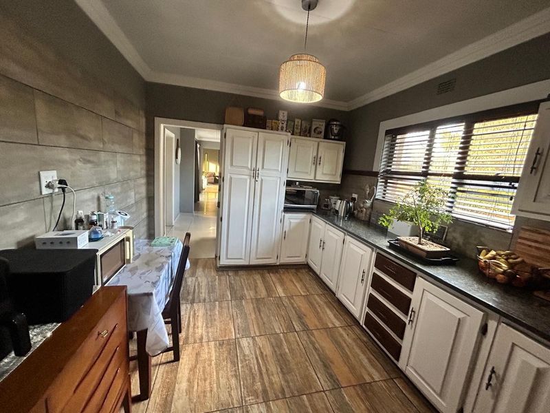 A functional kitchen featuring white cabinetry, stone countertops, wood-look floor tiles, and a pendant light fixture, offering a practical layout for daily use.