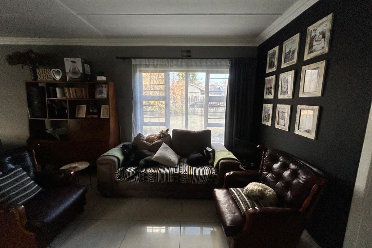 A living room featuring tiled flooring, a large window with security bars, and decorative ceiling cornicing.