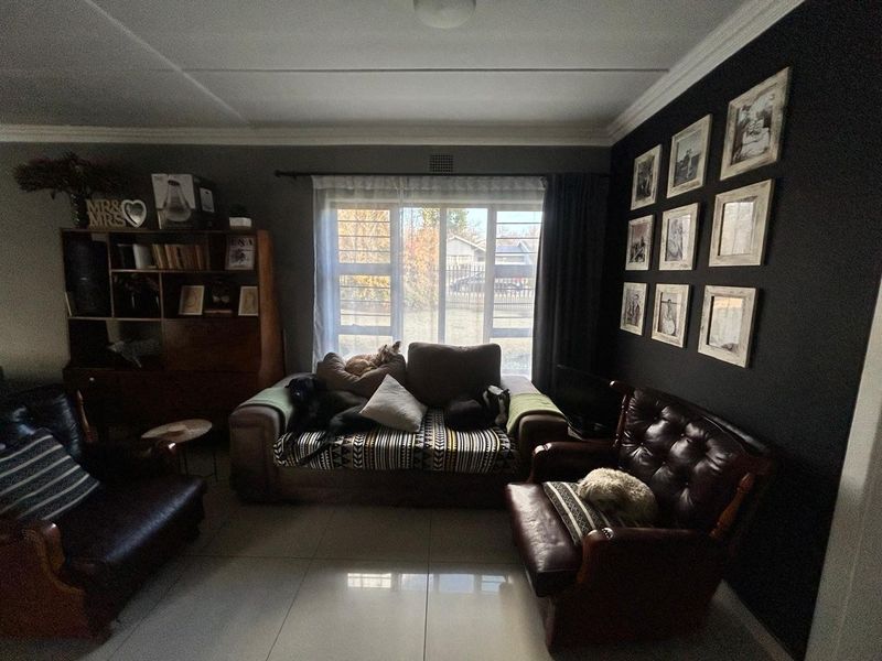 A living room featuring tiled flooring, a large window with security bars, and decorative ceiling cornicing.