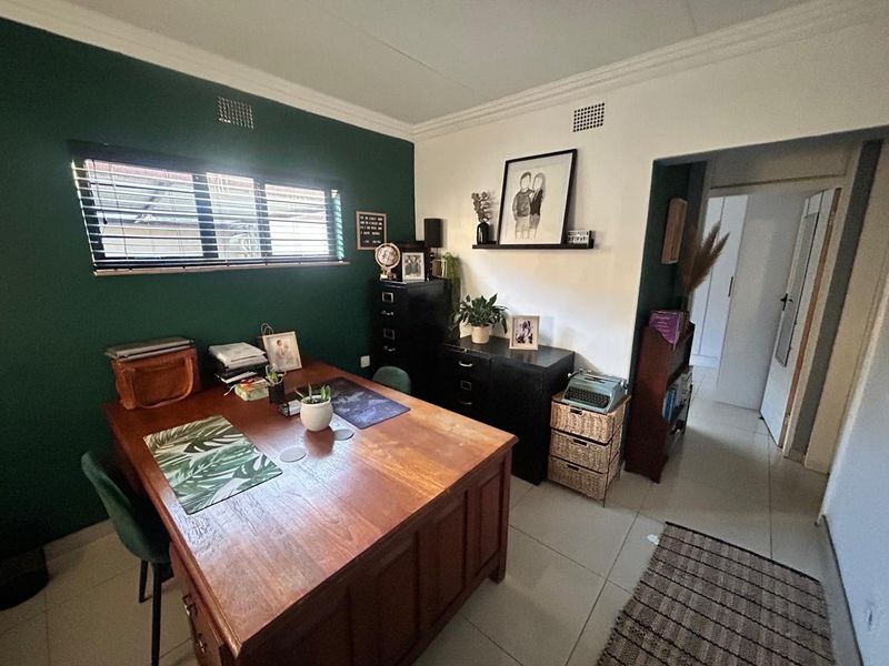 A functional home office featuring tiled flooring, decorative cornicing, and a window with venetian blinds, providing a comfortable workspace.