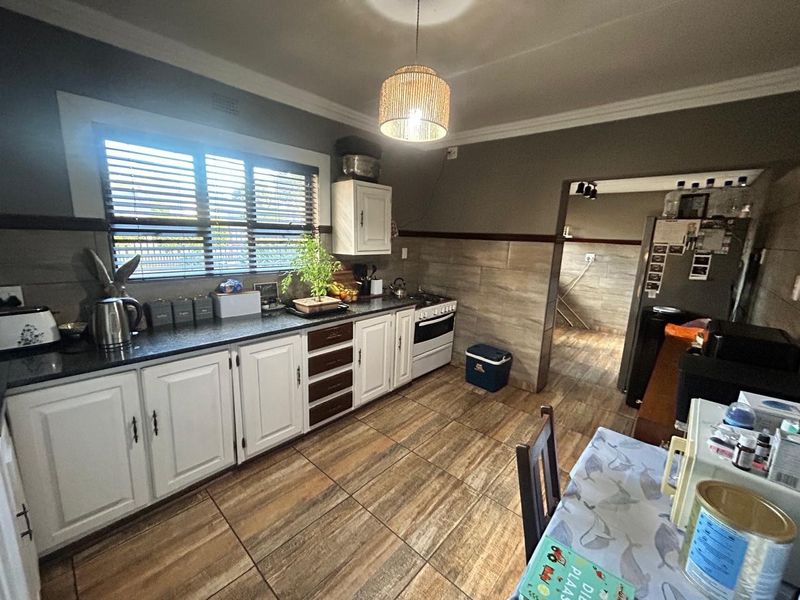 A functional kitchen featuring white cabinetry, dark stone countertops, tiled splashbacks, and wood-look floor tiles, with an adjacent scullery area.