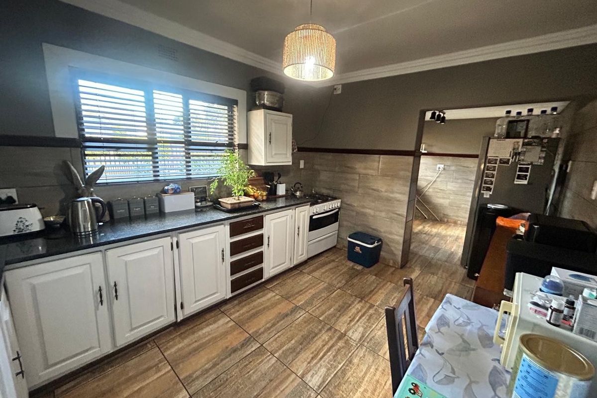 A functional kitchen featuring white cabinetry, dark stone countertops, tiled splashbacks, and wood-look floor tiles, with an adjacent scullery area.