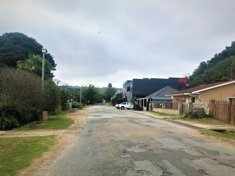 A view of the street approach showing the surrounding neighborhood, road surface, and adjacent residential and commercial properties.