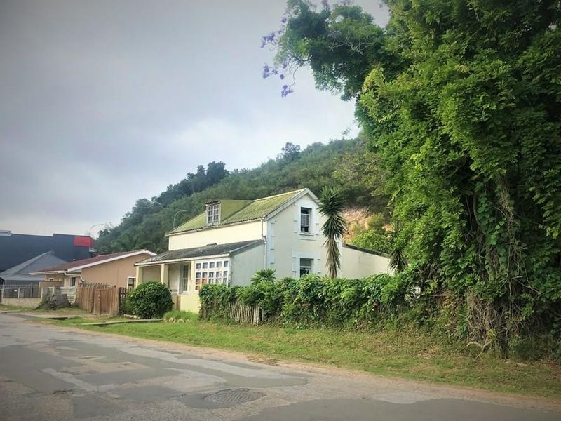 A detached house with a pitched roof and dormer window, situated on a street with mature trees and perimeter fencing.