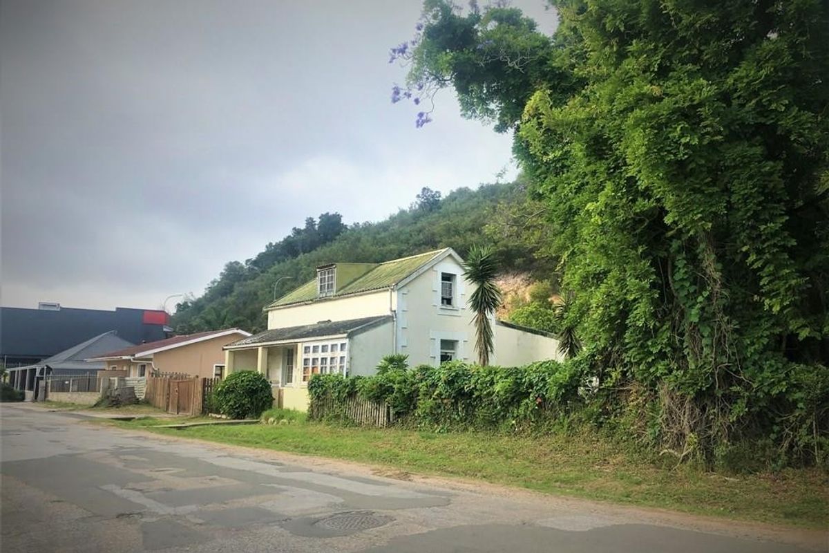 A detached house with a pitched roof and dormer window, situated on a street with mature trees and perimeter fencing.