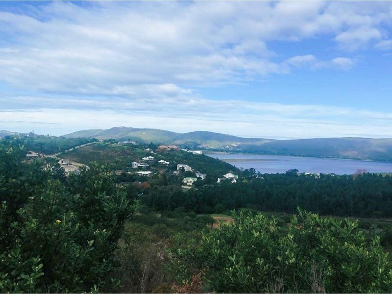 A scenic elevated view overlooking a coastal landscape, surrounding hills, and a body of water, showcasing the natural beauty of the area.