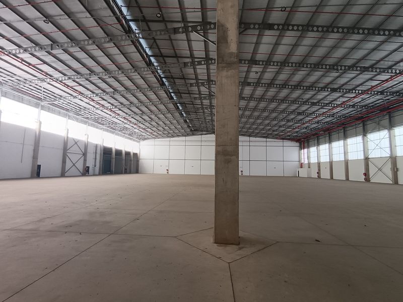 A large, open-plan industrial warehouse space featuring high ceilings with exposed steel trusses, concrete flooring, and integrated fire sprinkler systems.