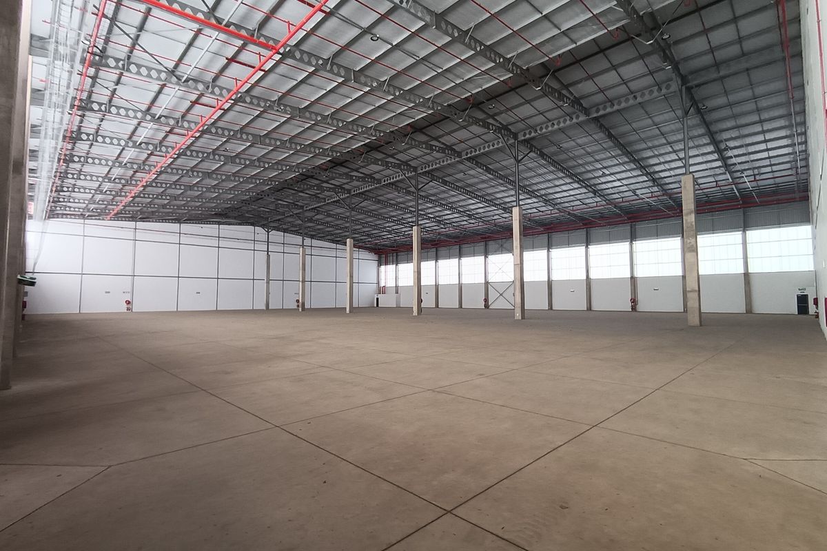 Spacious industrial warehouse featuring high ceilings, exposed steel truss roofing, fire sprinkler system, and durable concrete flooring, suitable for various commercial or storage operations.