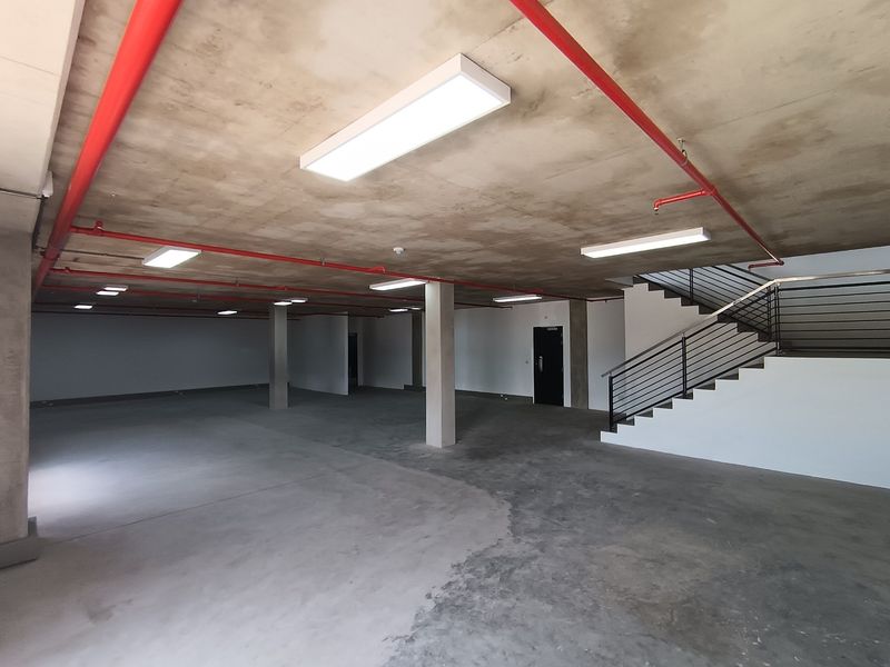 Spacious open-plan industrial area featuring exposed fire sprinkler systems, concrete flooring, and a modern staircase with metal railings.