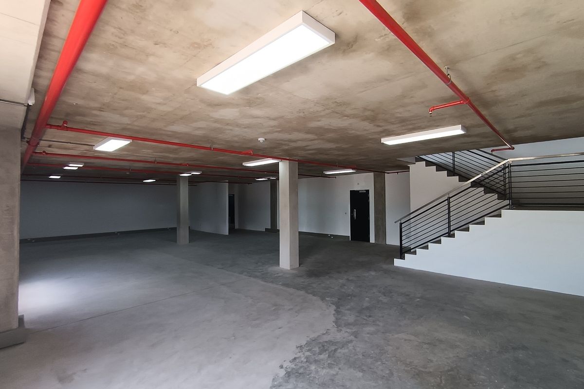 Spacious open-plan industrial area featuring exposed fire sprinkler systems, concrete flooring, and a modern staircase with metal railings.
