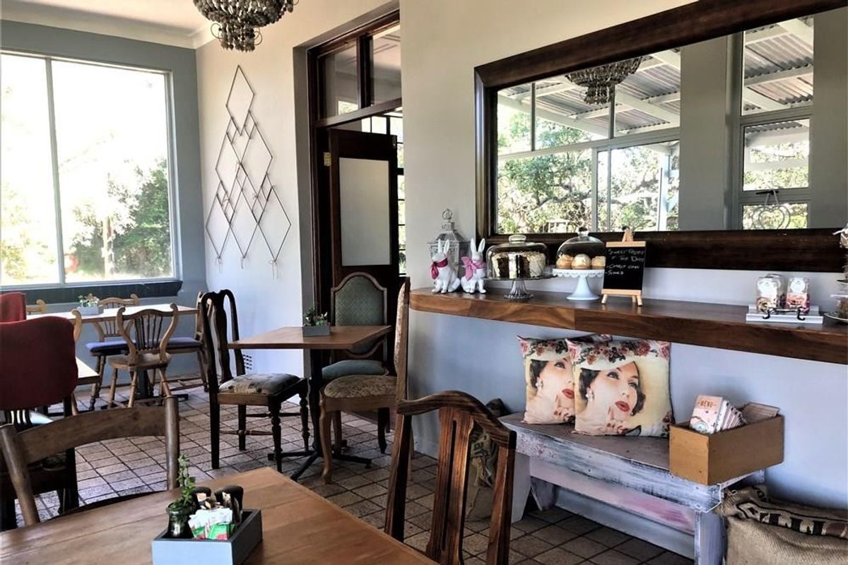 A bright commercial dining or lounge area featuring tiled floors, large windows, a built-in timber shelf, and a decorative wall mirror.