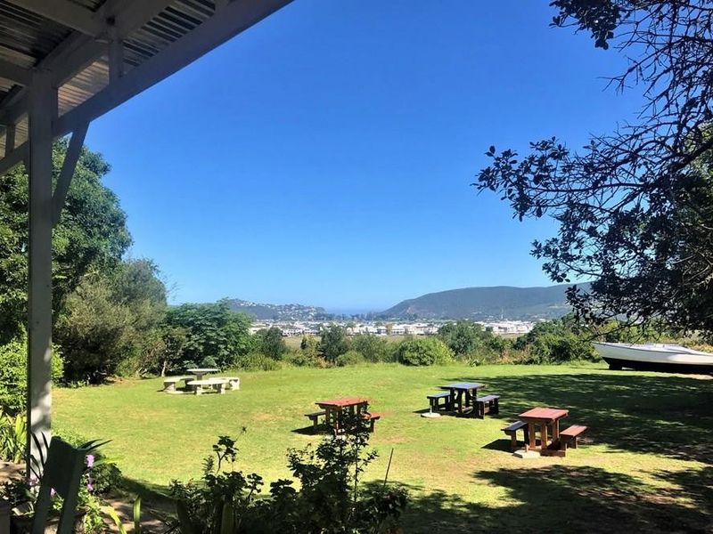 A covered patio area overlooking a spacious garden with scenic views of the surrounding landscape and distant town.