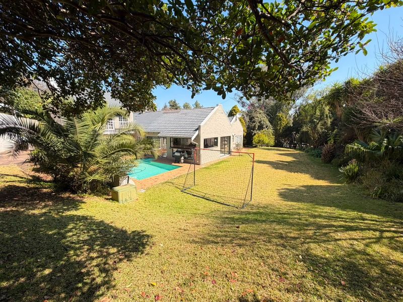 Rear view of the property featuring a swimming pool, paved patio area, and a spacious landscaped garden.