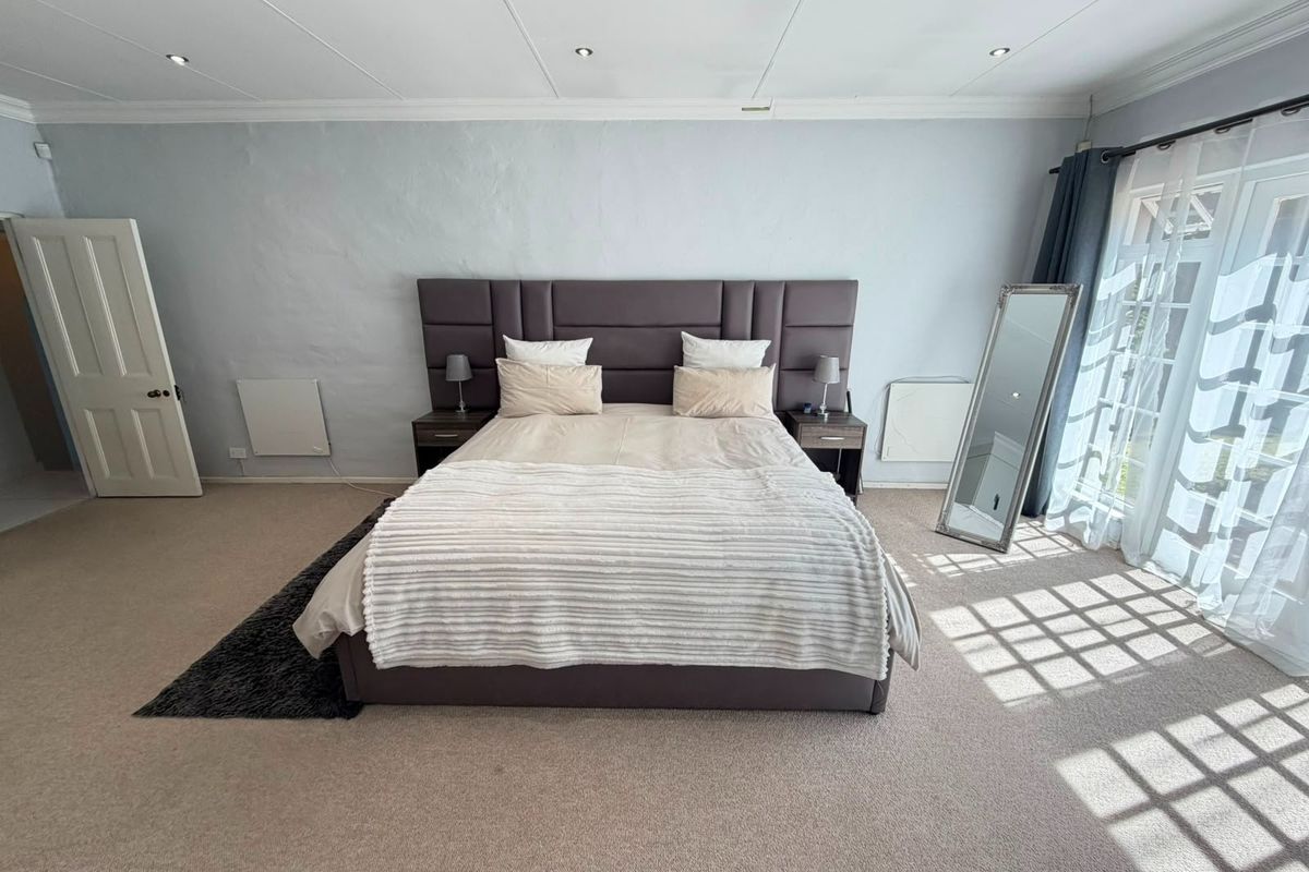Spacious bedroom featuring neutral carpeting, recessed downlighting, wall-mounted heating, and direct access to the outdoors through glass french doors.