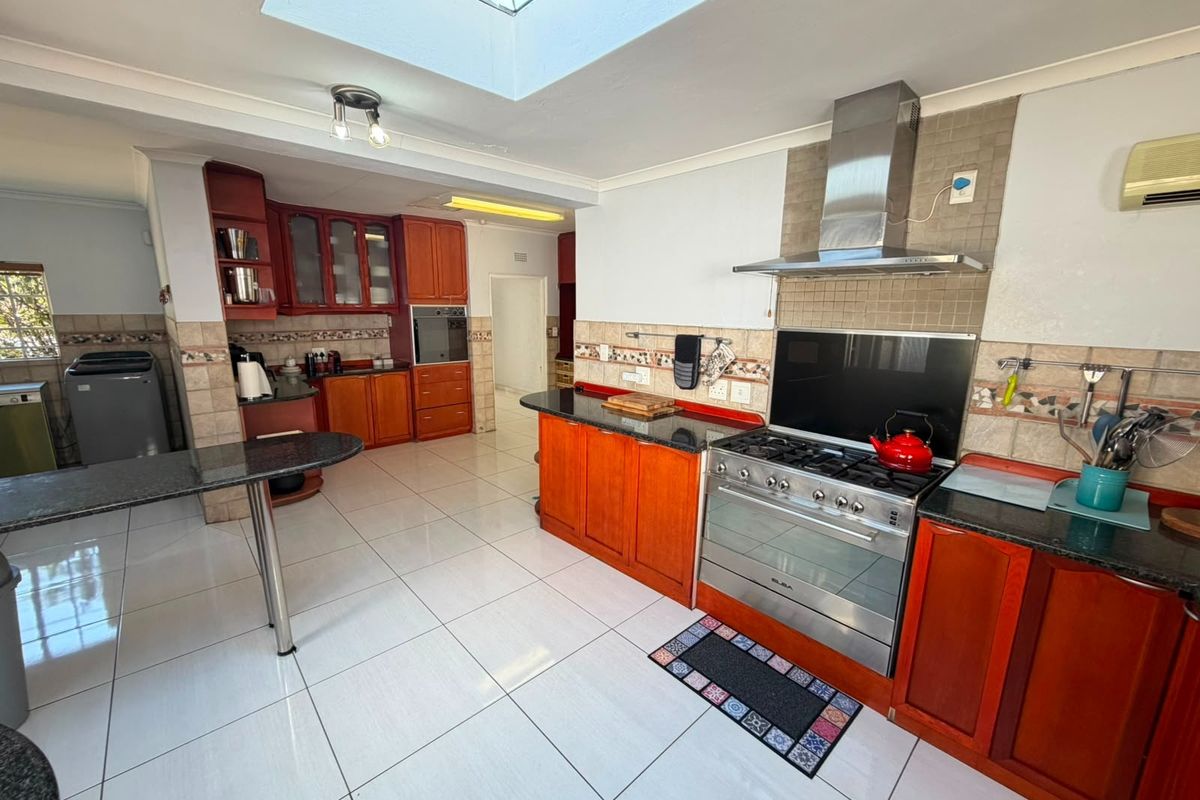 Spacious kitchen featuring warm wood cabinetry, granite countertops, a gas stove with extractor, and a large skylight providing ample natural light.