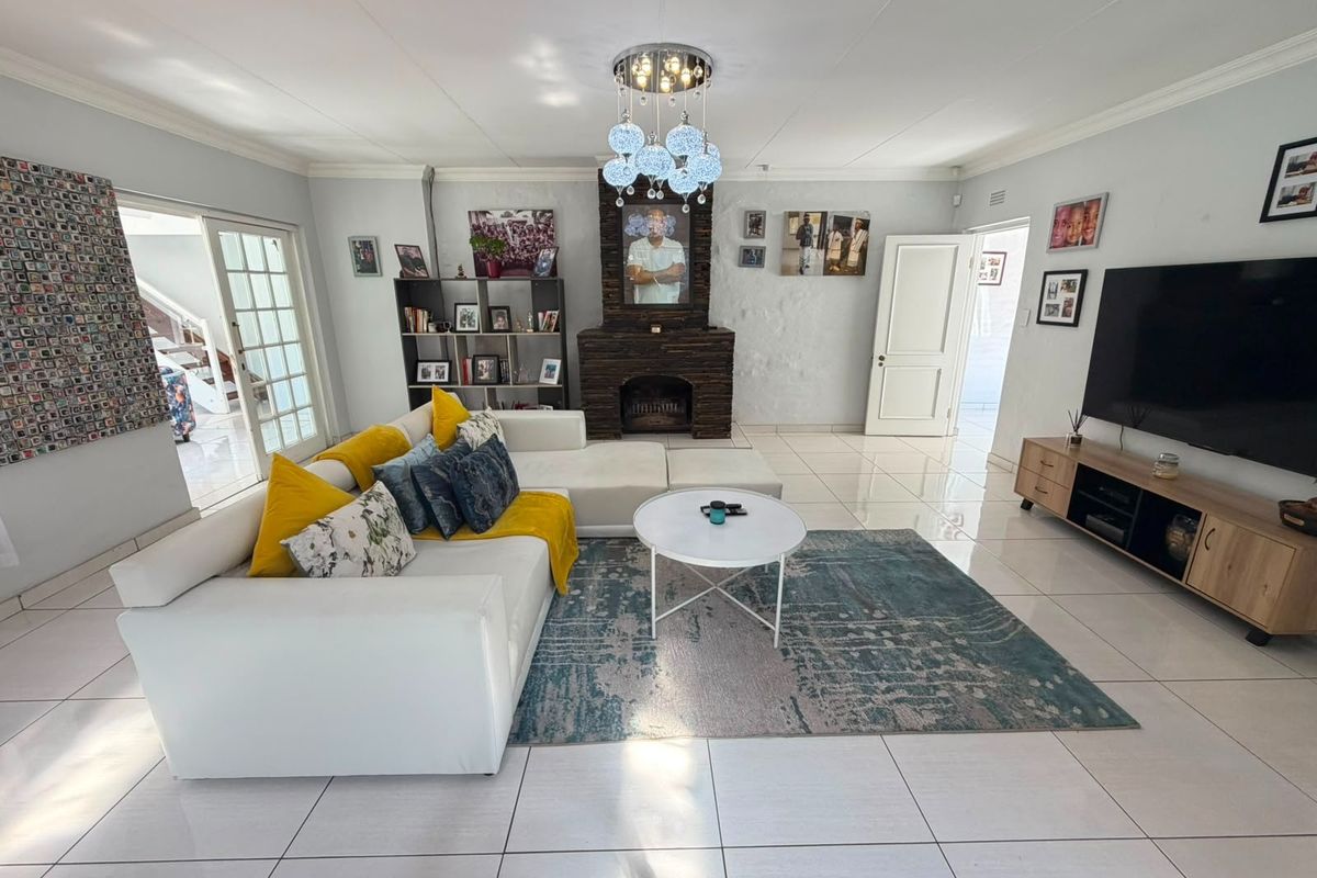 Spacious living room featuring large format floor tiles, a prominent stone-clad fireplace, and sliding glass doors providing access to adjacent areas.