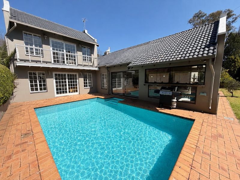 A well-maintained outdoor pool area featuring brick paving, a two-story building facade with a balcony, and large sliding doors leading to the interior.
