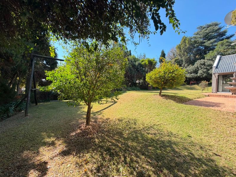 A spacious, well-maintained garden featuring a lush lawn, mature trees, and a brick-paved patio area adjacent to the house.