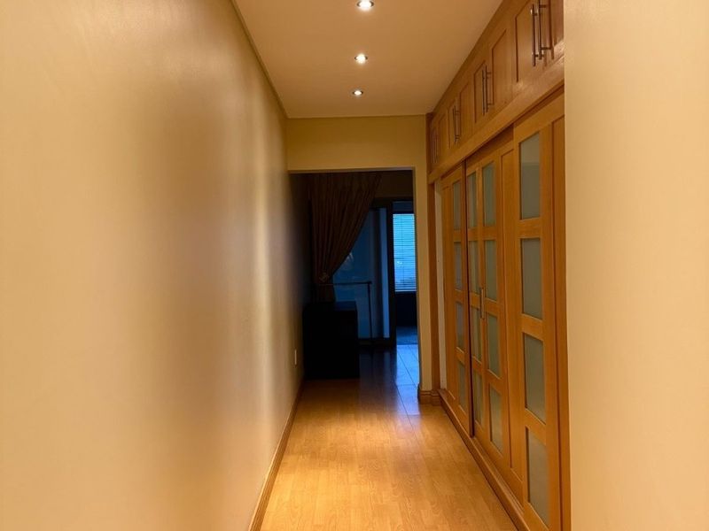 A well-lit hallway featuring extensive built-in wooden cabinetry with frosted glass panels and durable laminate flooring.