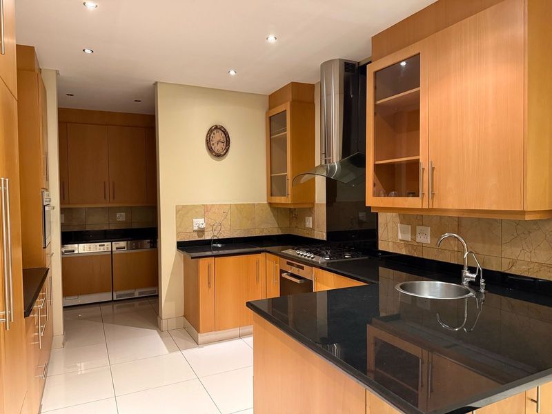 A well-maintained kitchen featuring light wood cabinetry, black granite countertops, built-in appliances, and tiled flooring with a functional layout.