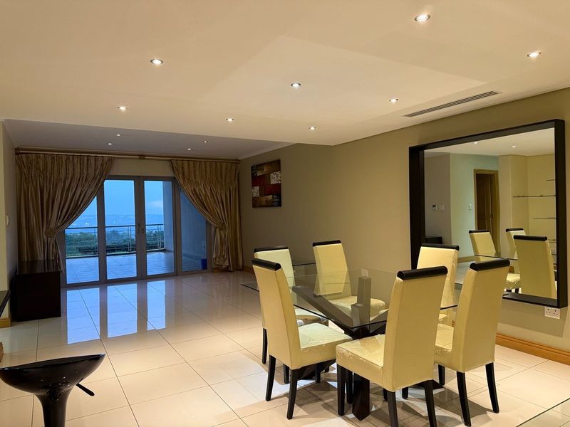 Spacious open-plan living and dining area featuring polished tile flooring, recessed lighting, and large sliding glass doors leading to a balcony with scenic views.
