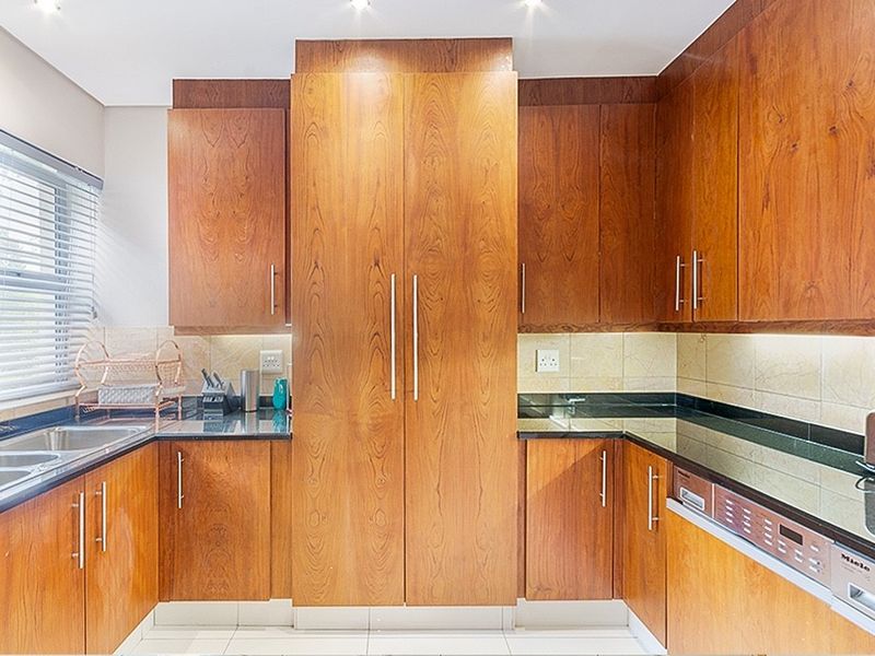 A well-maintained kitchen featuring warm wooden cabinetry, dark granite countertops, integrated dishwasher, and a tiled backsplash with modern recessed lighting.