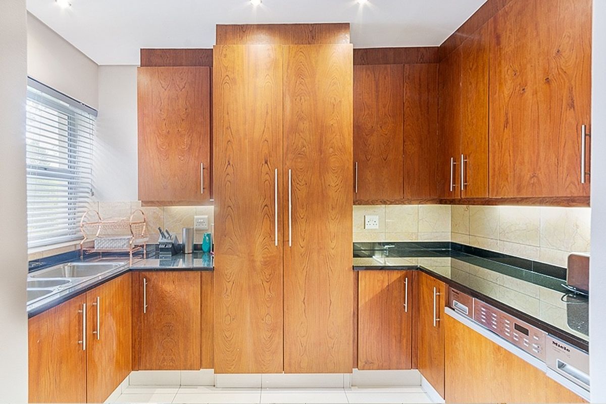 A well-maintained kitchen featuring warm wooden cabinetry, dark granite countertops, integrated dishwasher, and a tiled backsplash with modern recessed lighting.