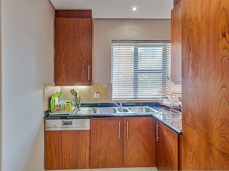 Compact kitchen featuring warm-toned wooden cabinetry, dark granite countertops, a double basin sink, and an integrated dishwasher.