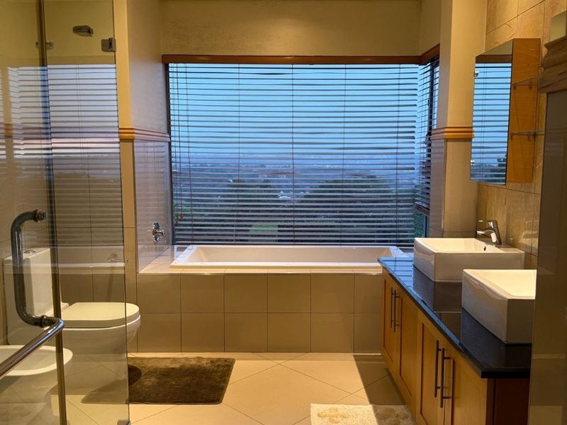 Modern bathroom featuring a double vanity with stone countertop, a built-in bathtub positioned by the window, and a separate glass-enclosed shower.