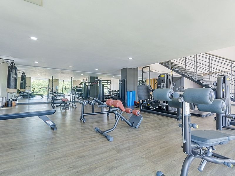 A well-maintained apartment gym featuring laminate flooring, recessed lighting, a full-length mirrored wall, and an integrated staircase.