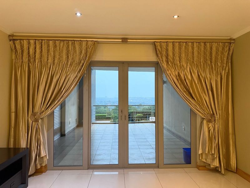 Bright living area featuring large double glass doors leading to an outdoor balcony with scenic views and neutral tiled flooring.