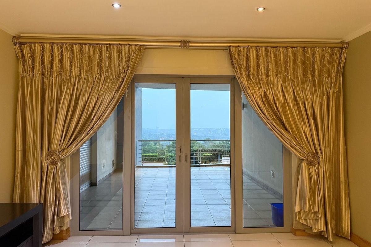 Bright living area featuring large double glass doors leading to an outdoor balcony with scenic views and neutral tiled flooring.