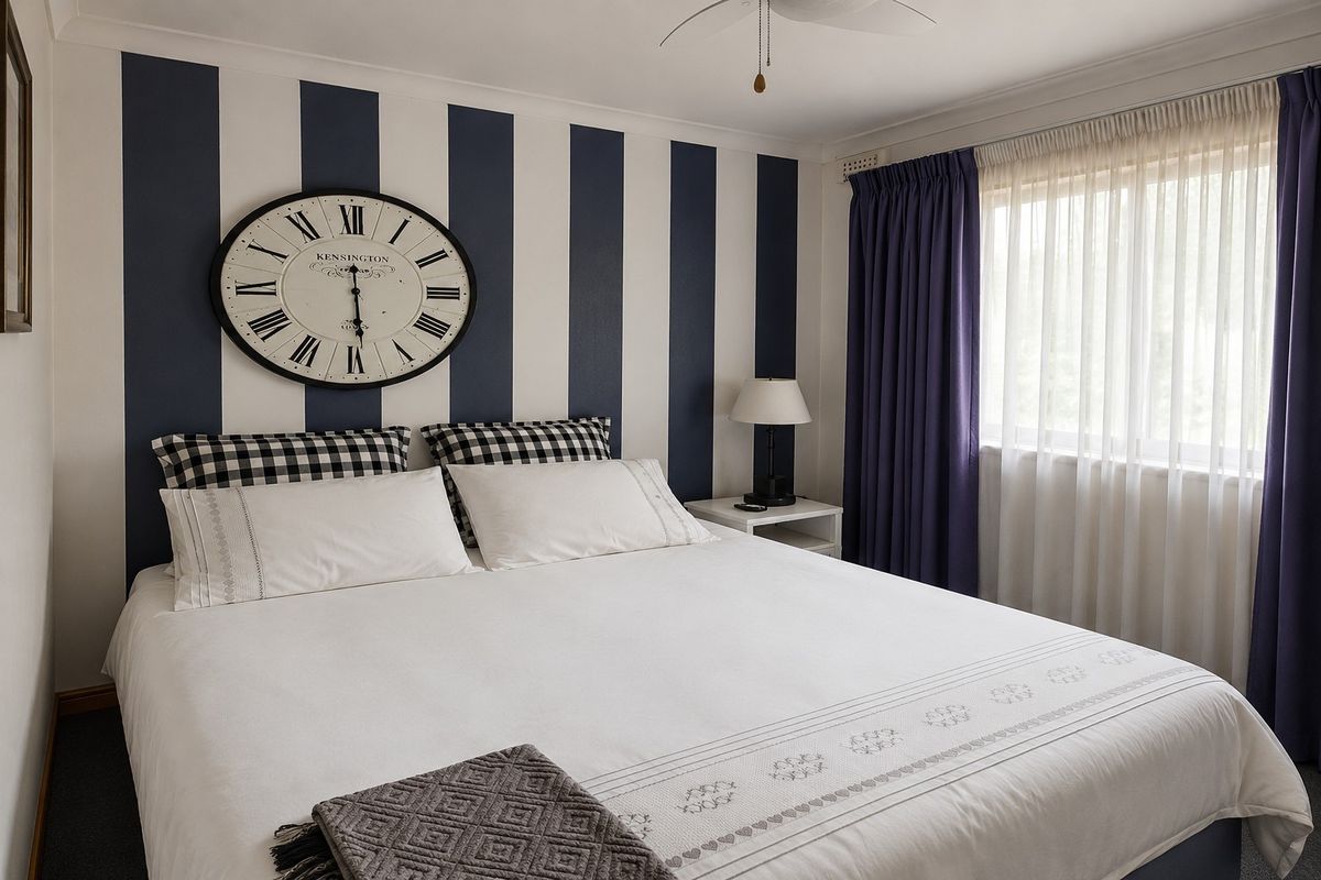 A well-maintained bedroom featuring a striped accent wall, ceiling fan, and window with layered curtains.