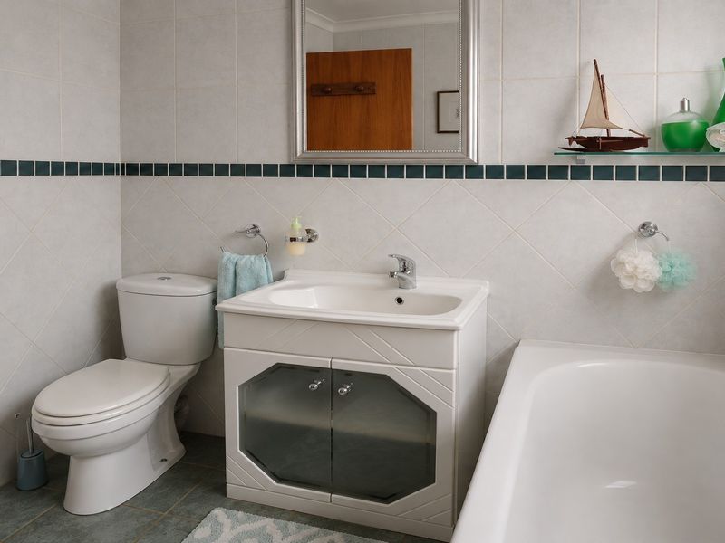 A functional bathroom featuring a vanity cabinet with basin, a standard toilet, and a bathtub, finished with neutral wall and floor tiling.