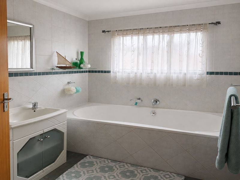 A functional bathroom featuring a built-in vanity with integrated sink, a tiled bathtub surround, and neutral wall tiling throughout.