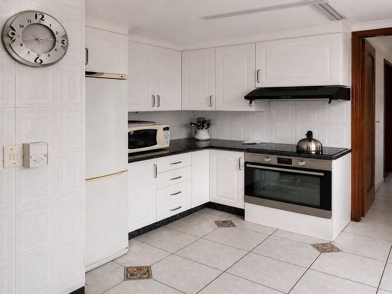 A functional kitchen featuring white cabinetry, granite countertops, built-in oven and hob, extractor fan, and tiled flooring with decorative accents.