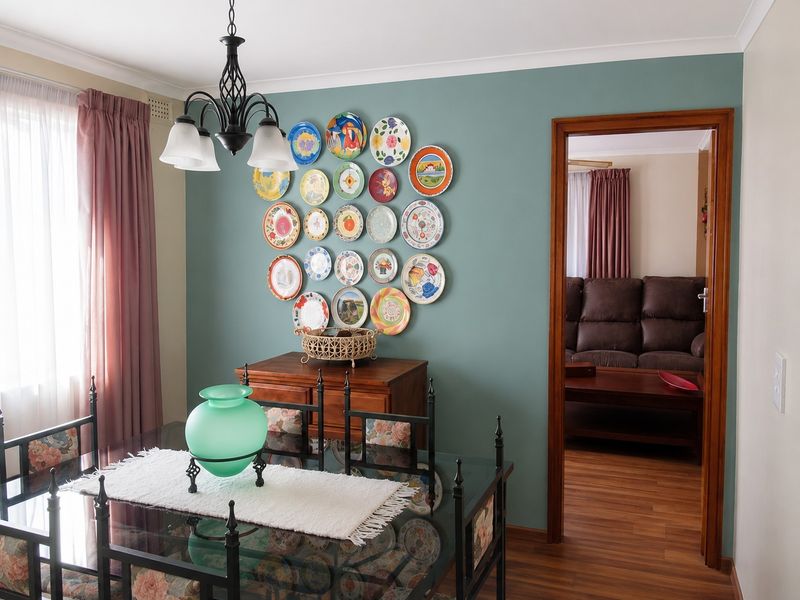 A well-maintained dining room featuring timber laminate flooring, decorative cornice, and a classic wrought iron chandelier, with a clear view into the adjacent living area.