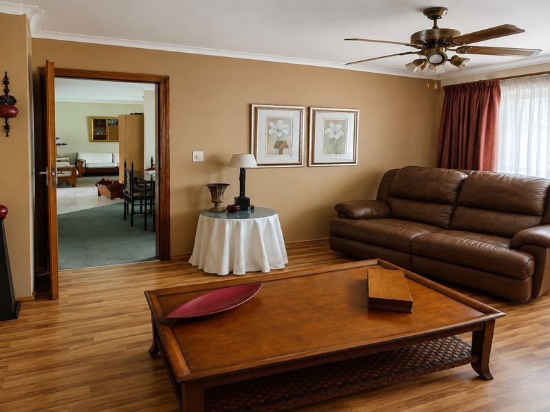 A comfortable living room featuring laminate flooring, a ceiling fan, and coved cornicing, with a doorway leading to an adjacent living space.