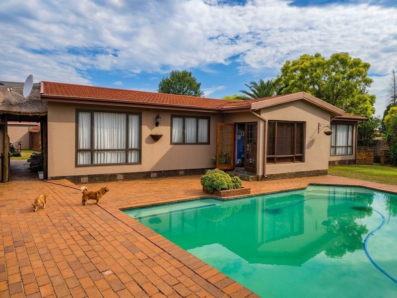 A well-maintained rear exterior view featuring a swimming pool, brick paved patio area, and a single-story house with a tiled roof.