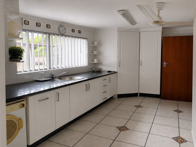 A functional kitchen featuring white cabinetry, dark granite countertops, tiled flooring, and a ceiling fan, offering ample storage and workspace.