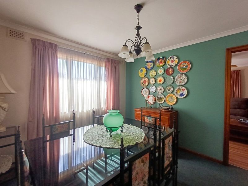A dining room featuring a green accent wall, ceiling light fixture, and large window with curtains.