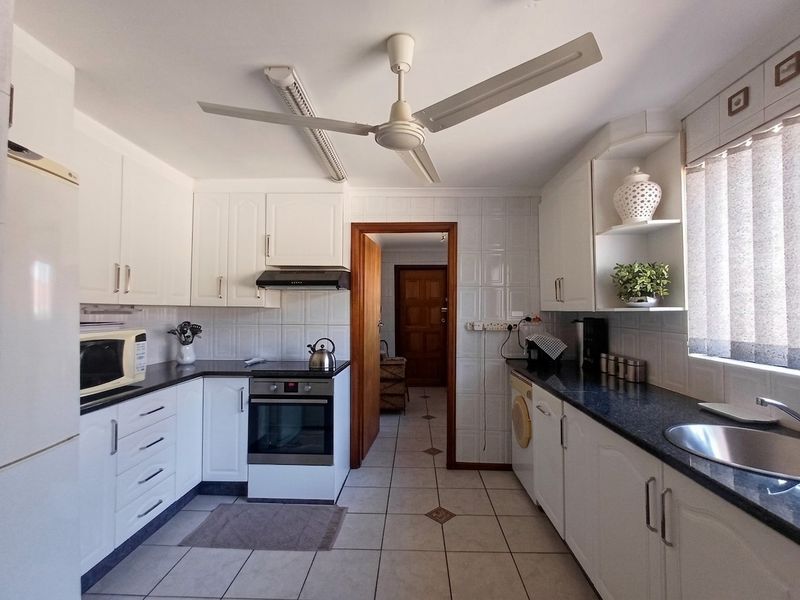 A functional kitchen featuring white cabinetry, dark countertops, tiled backsplash, and integrated appliances, providing a clean and practical workspace.