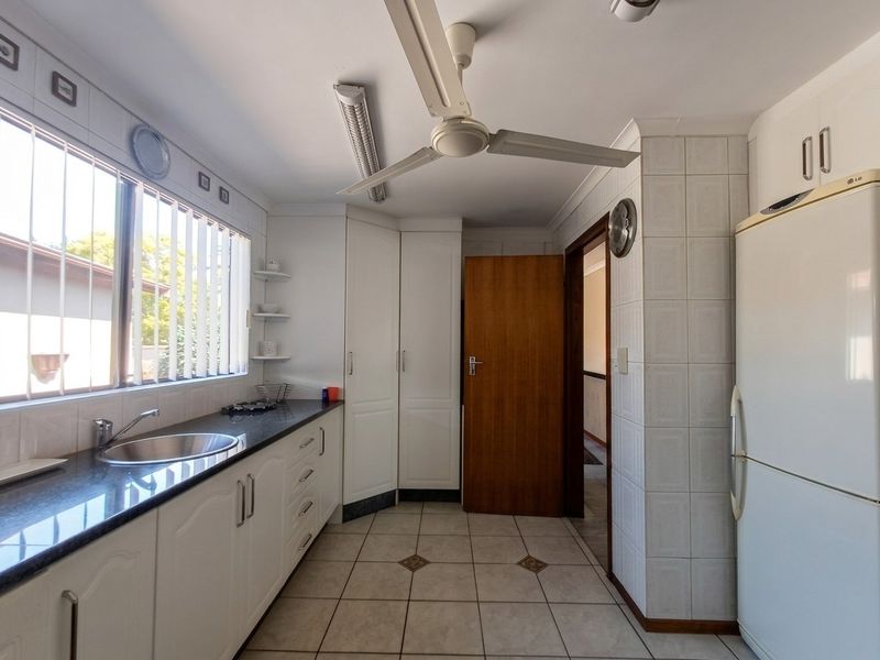 Functional kitchen featuring white built-in cabinetry, dark laminate countertops, stainless steel sink, and tiled flooring with a ceiling fan.