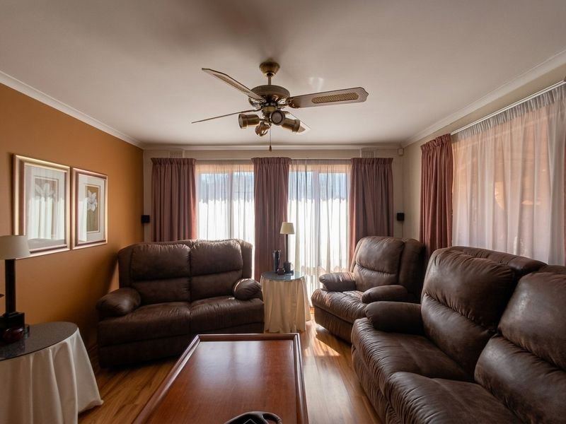 A comfortable living room featuring hardwood flooring, a central ceiling fan, and large sliding glass doors that provide ample natural light.
