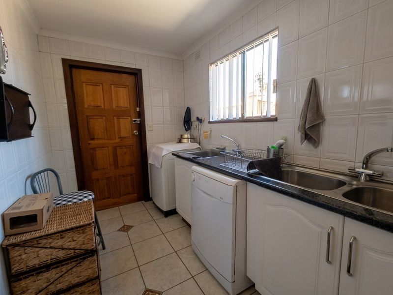 Functional laundry room featuring tiled walls, tiled flooring, built-in cabinetry with laminate countertops, and a double stainless steel sink.