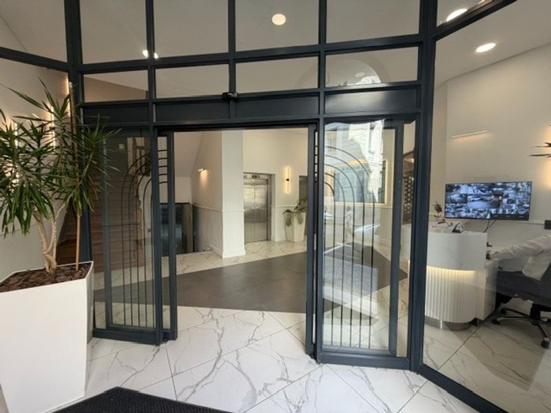 Modern office building entrance featuring a glass partition, marble-look flooring, and a professional reception area with elevator access.