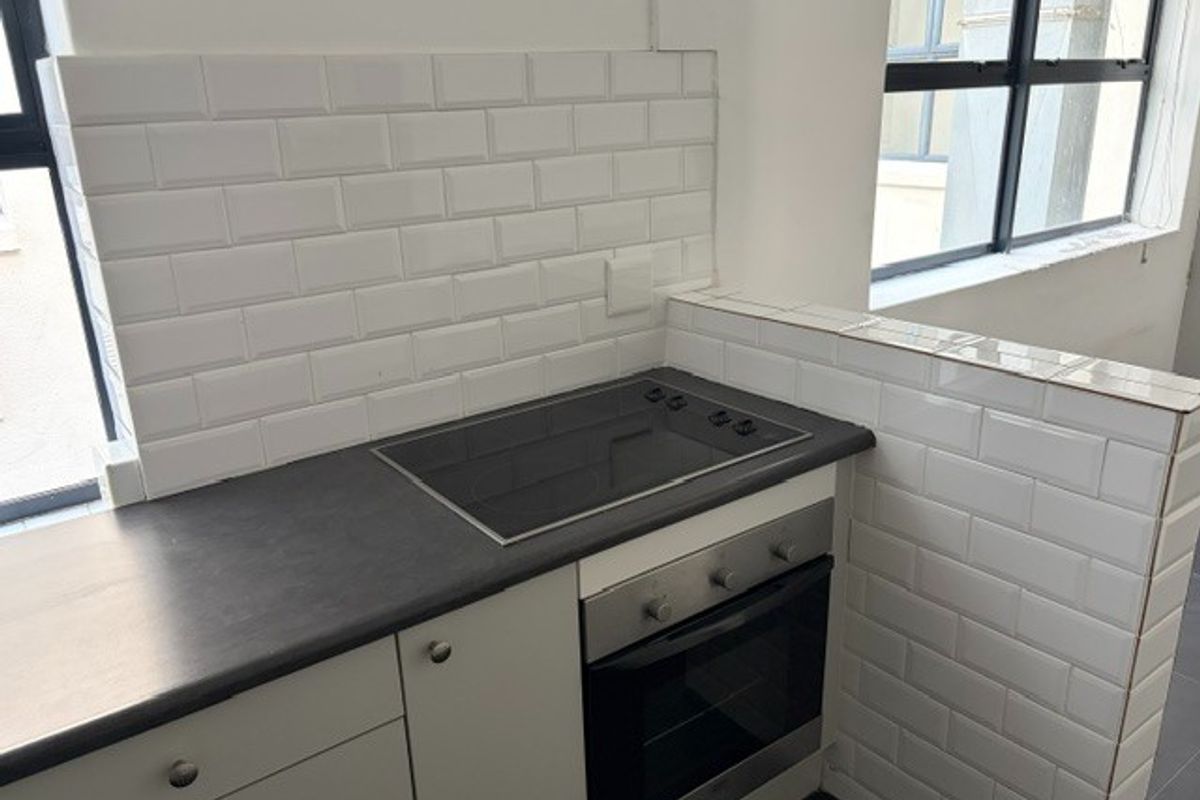 A compact, modern kitchen area featuring a built-in oven, electric hob, dark laminate countertops, and a clean white subway tile backsplash.